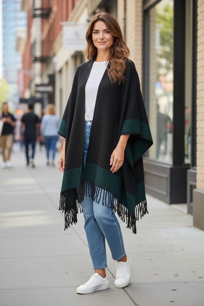 Front view of the reversible black and emerald green wool blend ruana wrap with fringe, styled with a white top, light-wash jeans, and white sneakers.