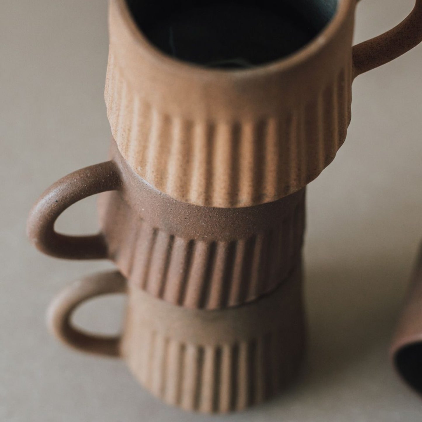 Close up of stacked fluted terracotta mugs showing textured ridged surface