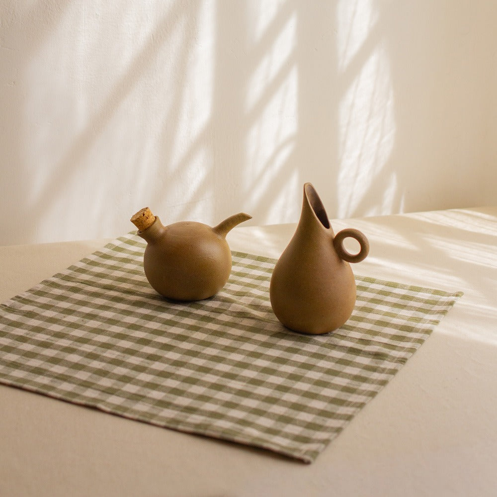 Ceramic oil and vinegar cruet set with cork stopper, styled on a green gingham cloth in warm natural light