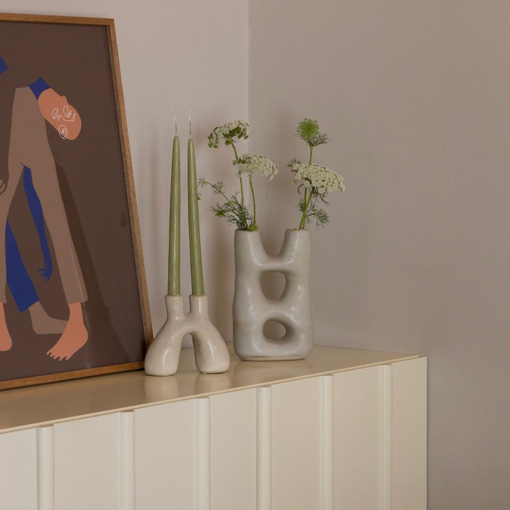 Off-white double-portal ceramic vase styled on a console table with tapered candles, artwork, and fresh greenery.