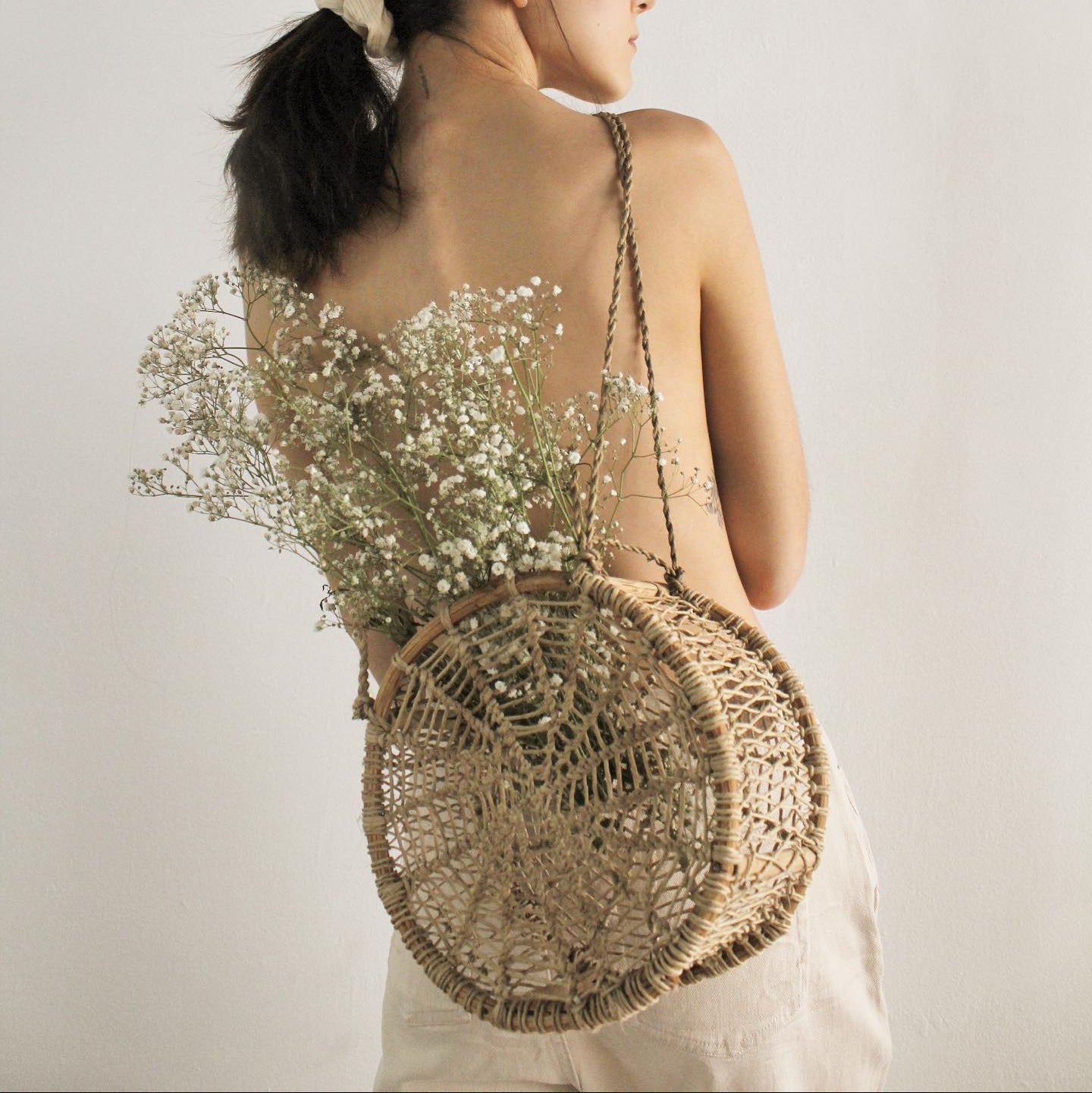 Back view of woman wearing artisan circular jonote basket bag filled with flowers