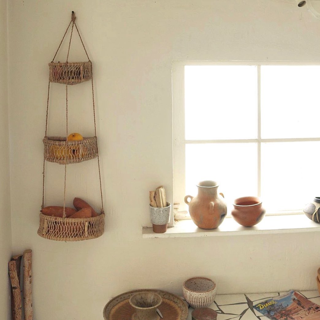 Three-tier woven hanging basket displayed beside a rustic window with clay pottery