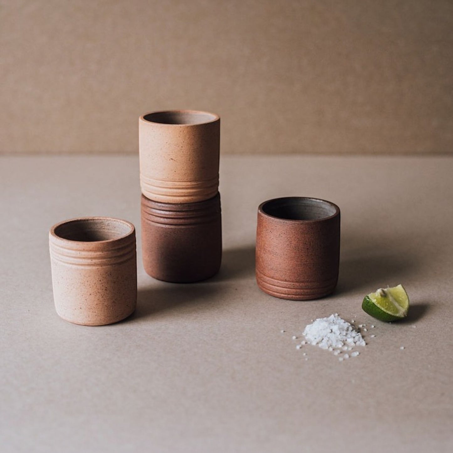 Set of handmade Mexican ceramic shot glasses for tequila or mezcal styled with lime and salt on a neutral surface
