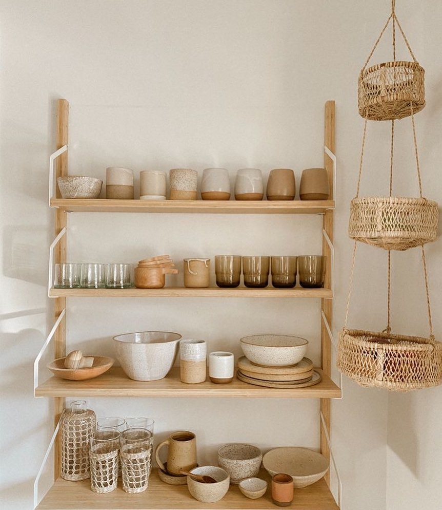 Three-tier woven hanging basket shown beside wooden shelving with pottery.
