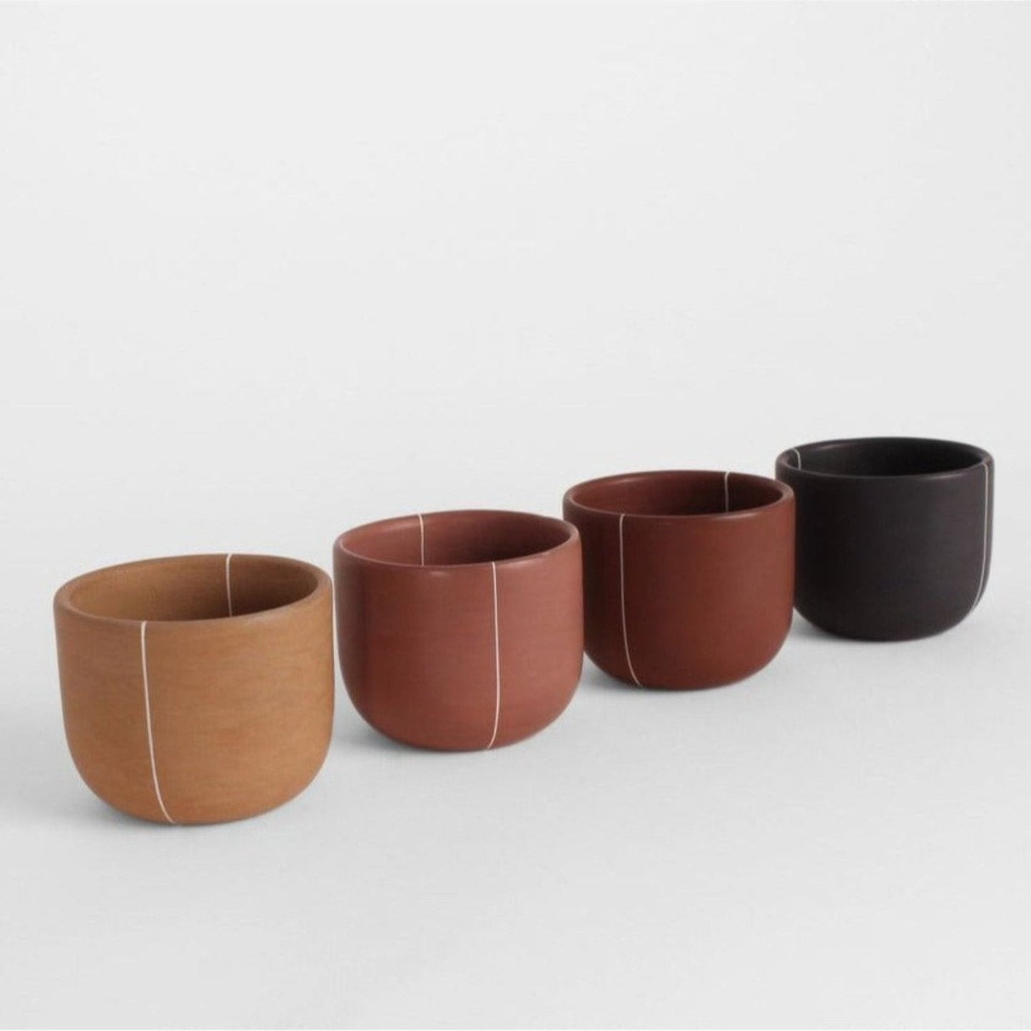 Artisanal burnished clay cups in four colors stacked together on a neutral background