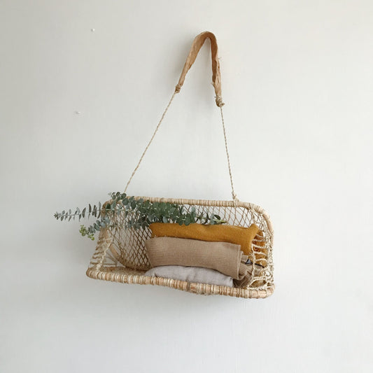 Handwoven jonote hanging basket with eucalyptus and textiles displayed on a white wall.