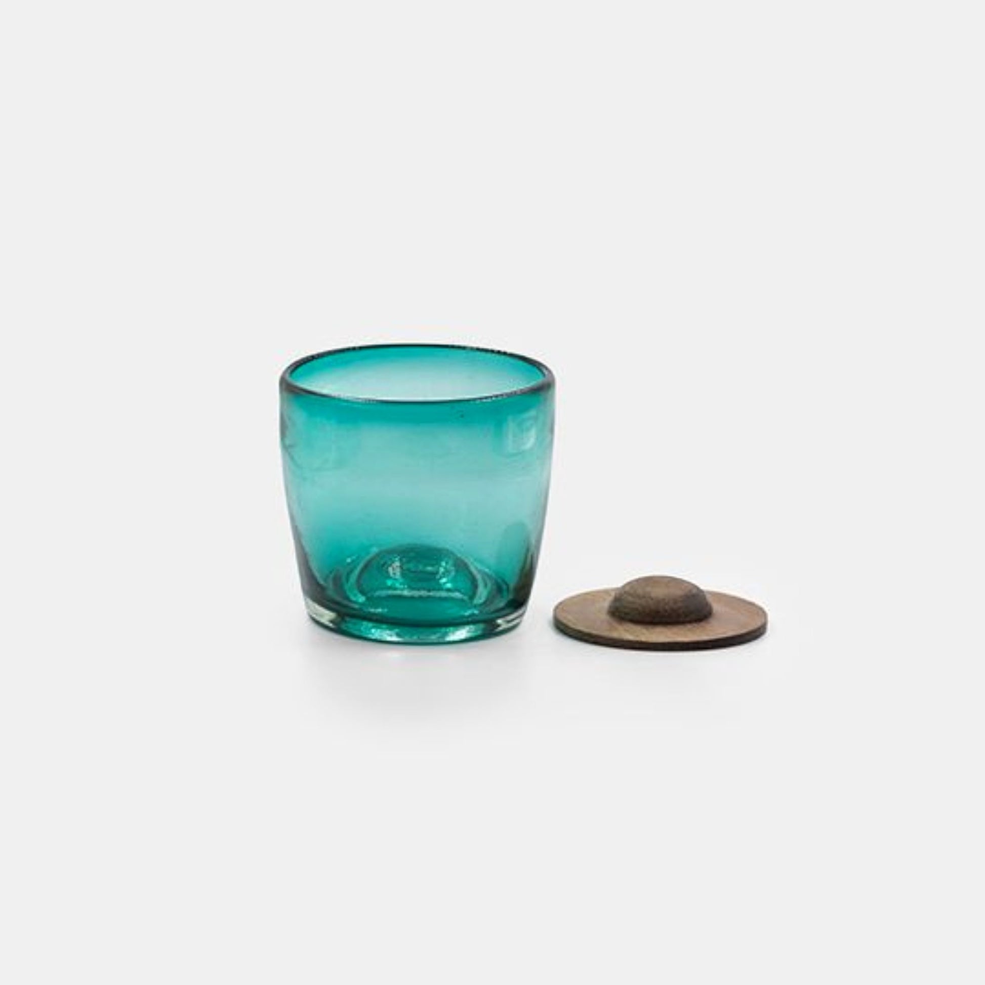 Turquoise glass tumbler next to a parota wood coaster on a white background.