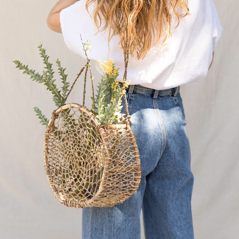 Woman carrying a handwoven circular jonote basket bag with greenery, artisan-made in Mexico