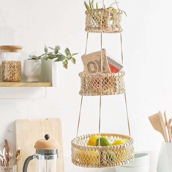 Three-tier woven hanging basket used for kitchen storage with fruit and small items.