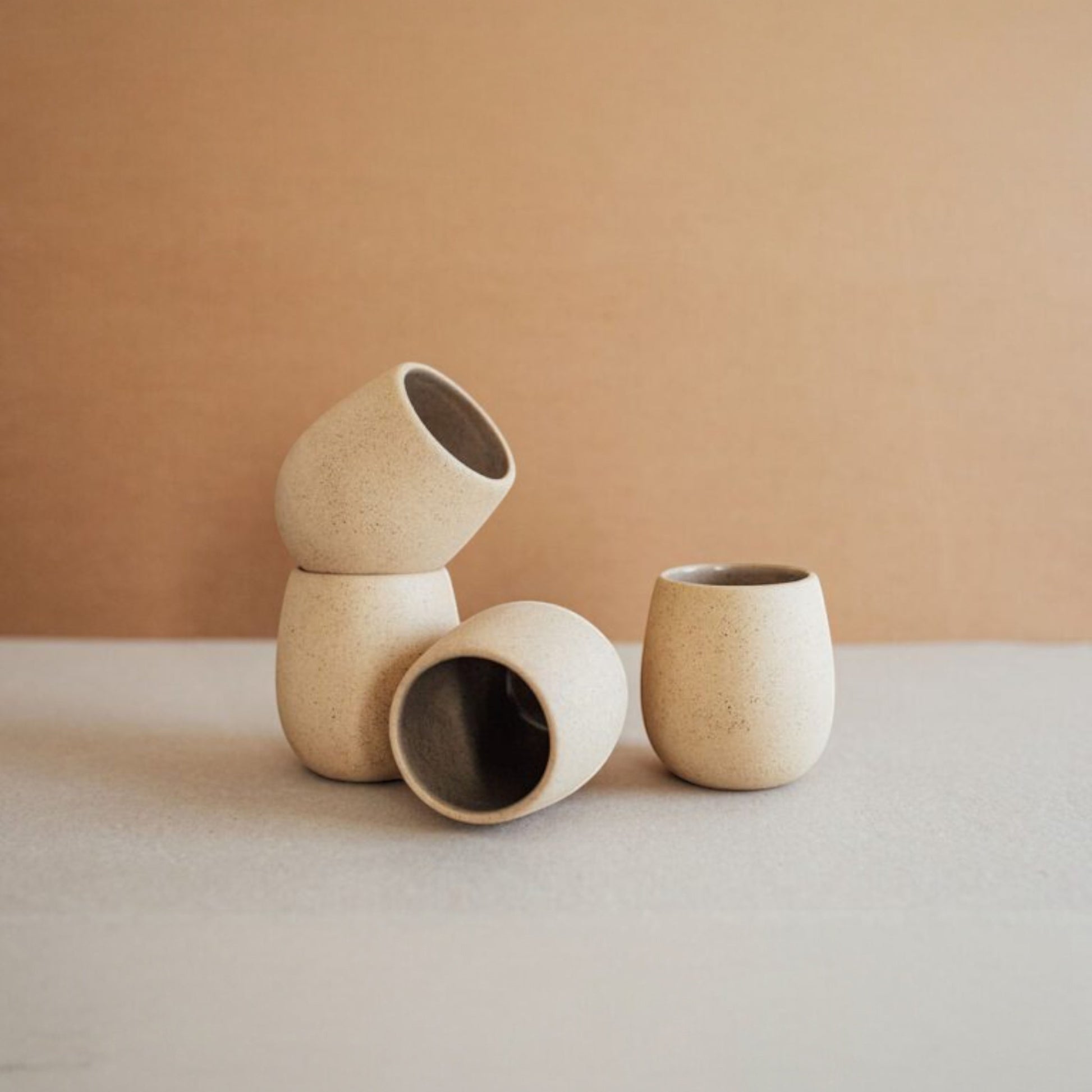 Four sand-colored round ceramic cups grouped together on a neutral backdrop.