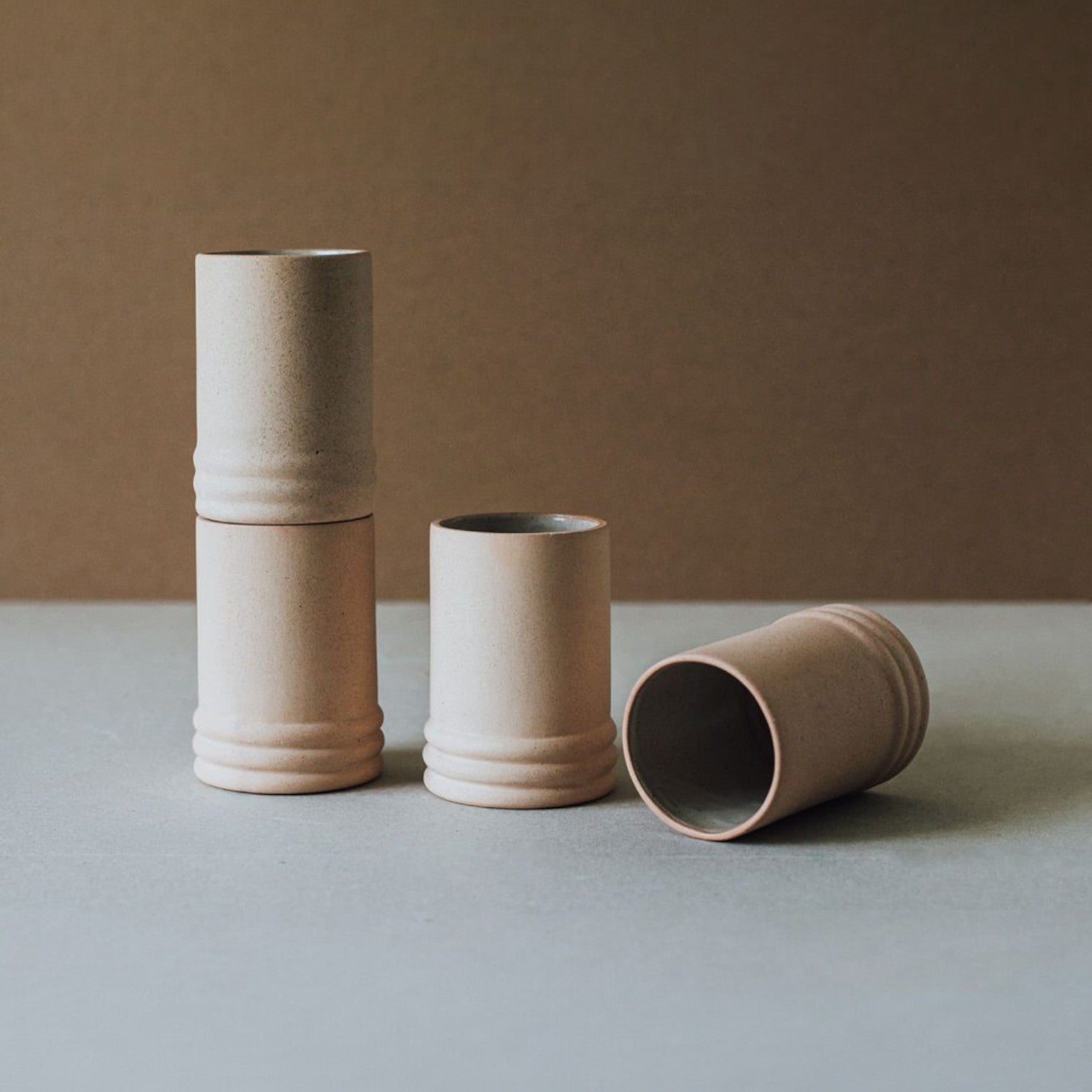 Four ceramic cups in beige tones on a gray surface with a brown backdrop