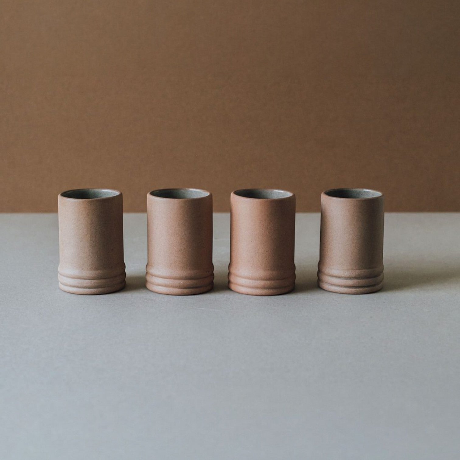 Four ceramic cups of slightly different heights arranged in a row on a neutral background