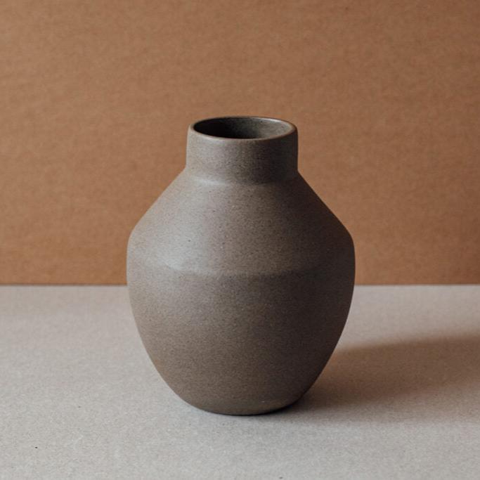 Round terracotta ceramic vase in chocolate and sand tones on neutral background.