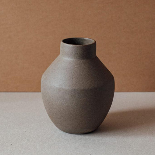 Round terracotta ceramic vase in chocolate and sand tones on neutral background.