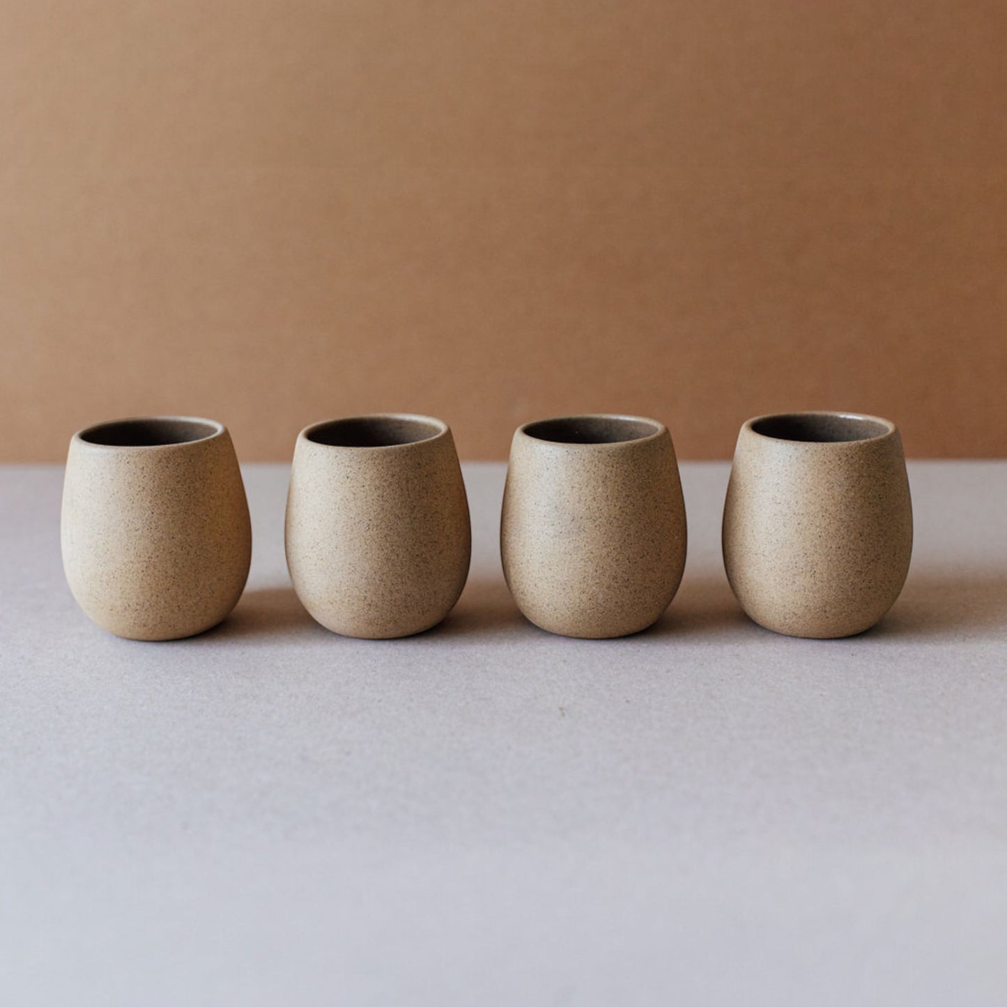 Four round ceramic cups in sand tones lined up on a neutral background.