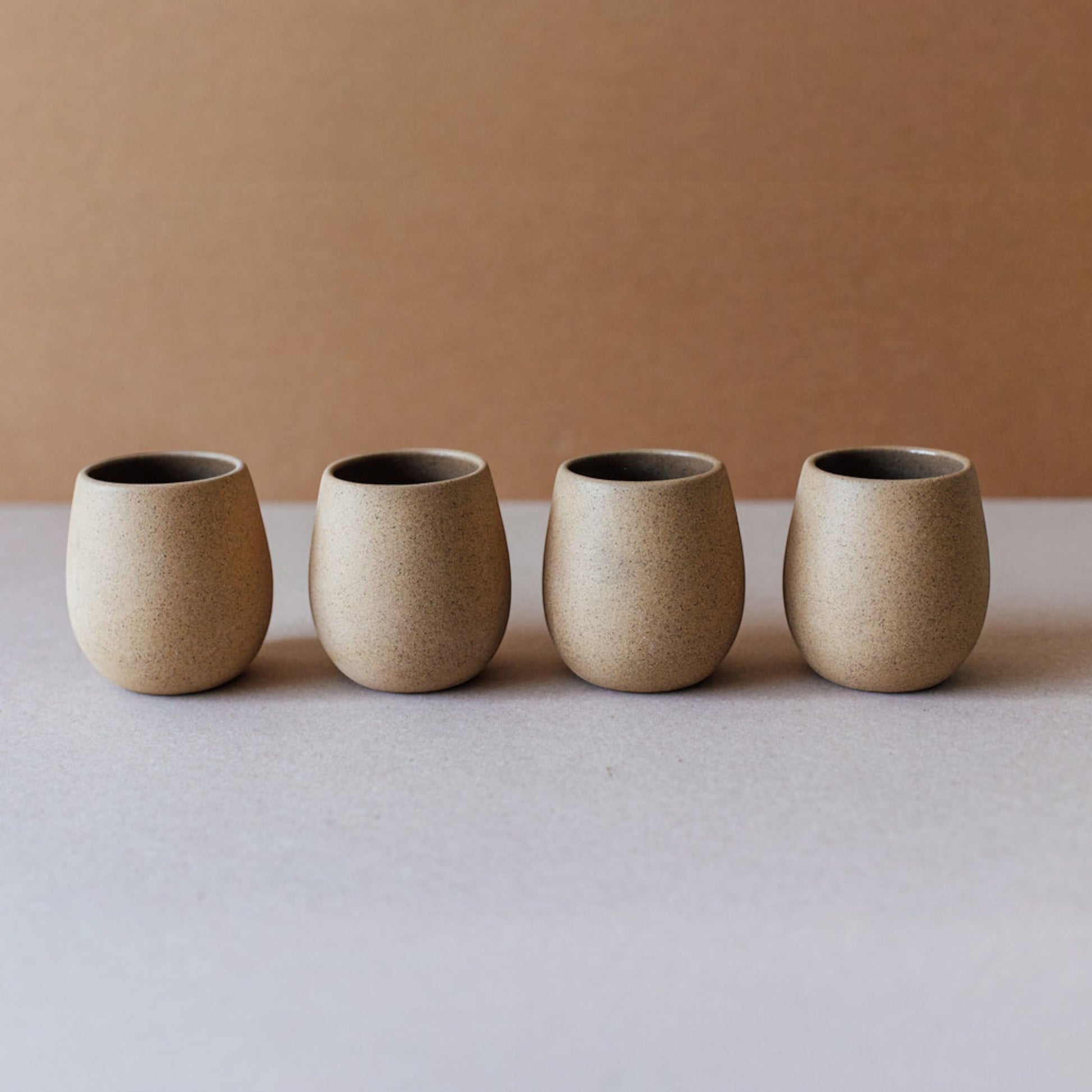 Four round ceramic cups in sand tones lined up on a neutral background.