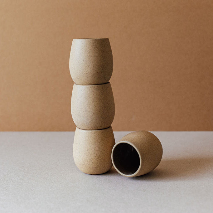 Three stacked sand-colored round ceramic cups with one lying on its side.