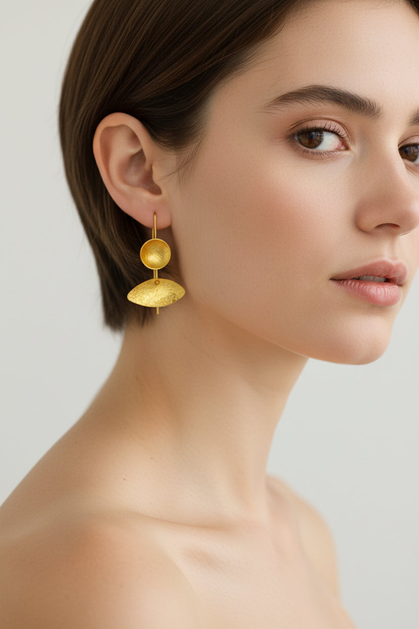 Woman wearing asymmetrical gold sculptural drop earrings, side view