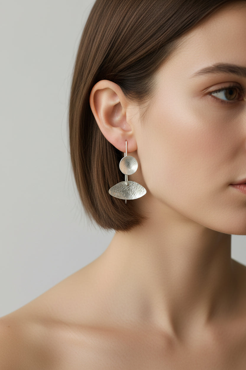 Woman wearing asymmetrical silver sculptural drop earrings, side view