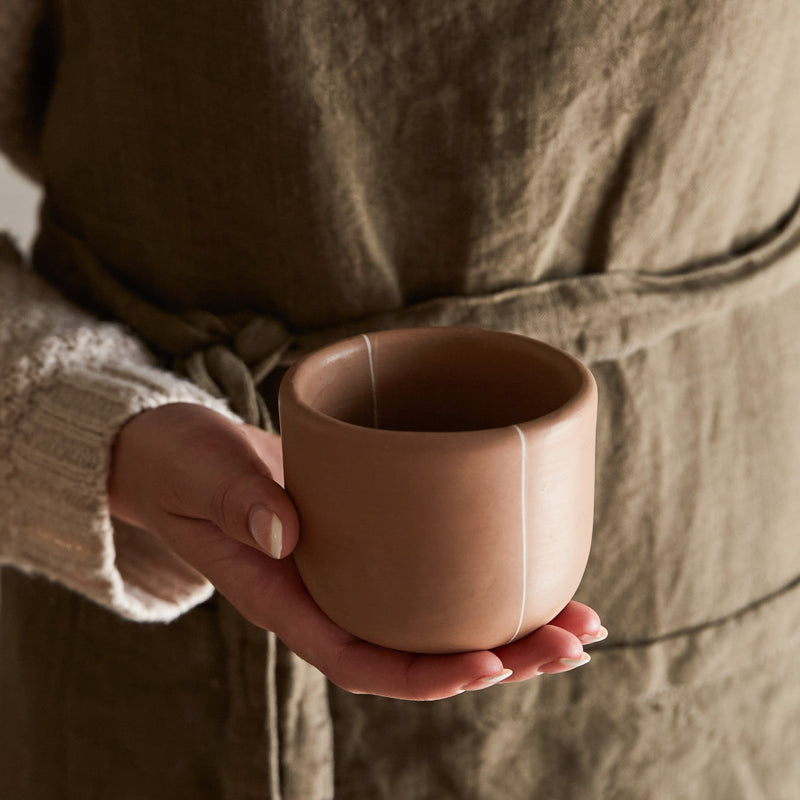Handmade clay cup held in hand showing size and matte burnished finish