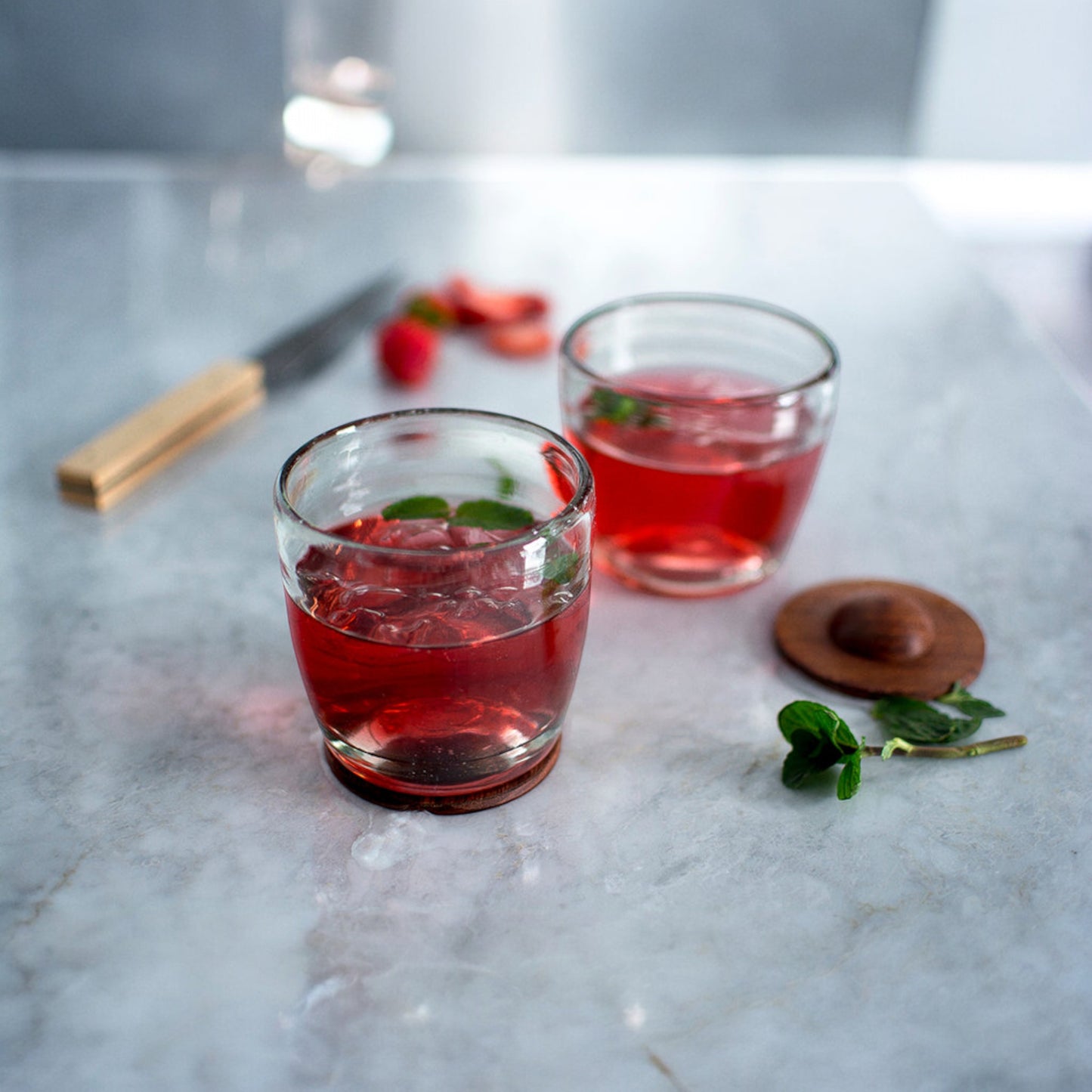 Two glass tumblers with red iced cocktails and mint leaves on a marble surface.