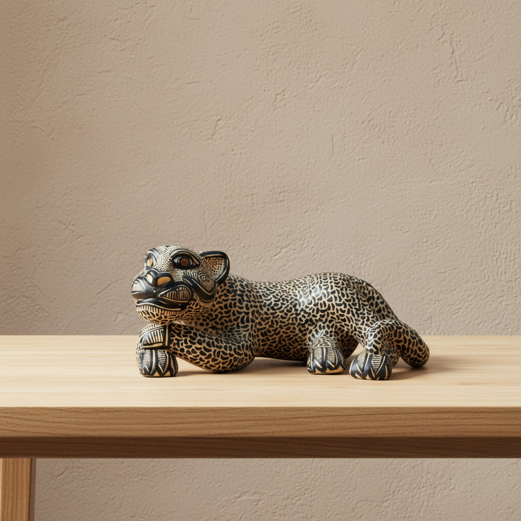 A hand-painted beige ceramic Mayan jaguar sculpture displayed on a light wood table against a warm beige wall.
