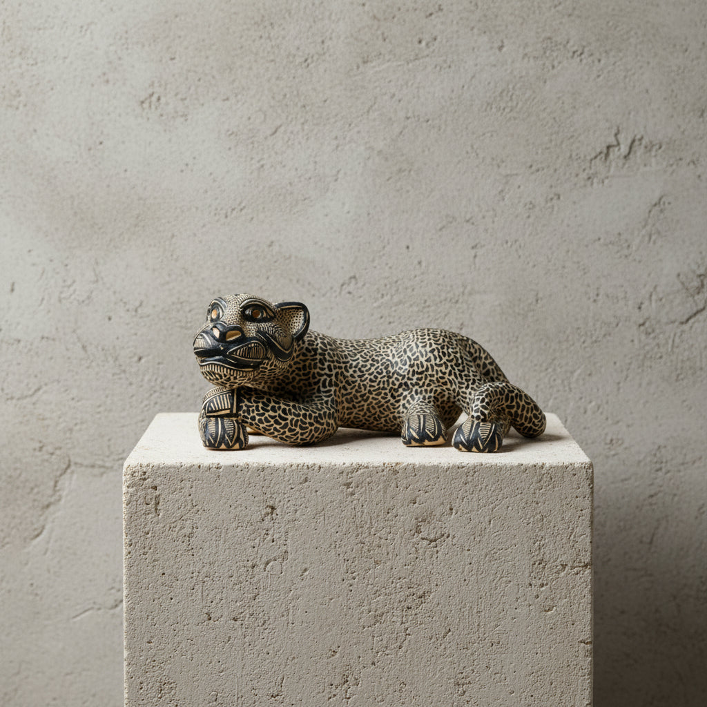 A hand-painted beige ceramic Mayan jaguar sculpture resting on a light stone pedestal against a textured neutral wall.
