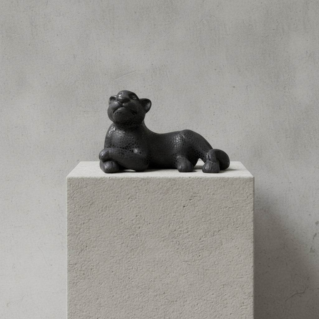 Handmade black jaguar ceramic sculpture on stone pedestal, minimalist background