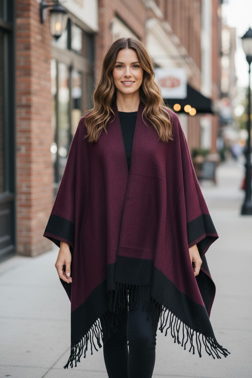 Front view of a reversible burgundy and black wool blend ruana wrap with fringe, styled over a black outfit.