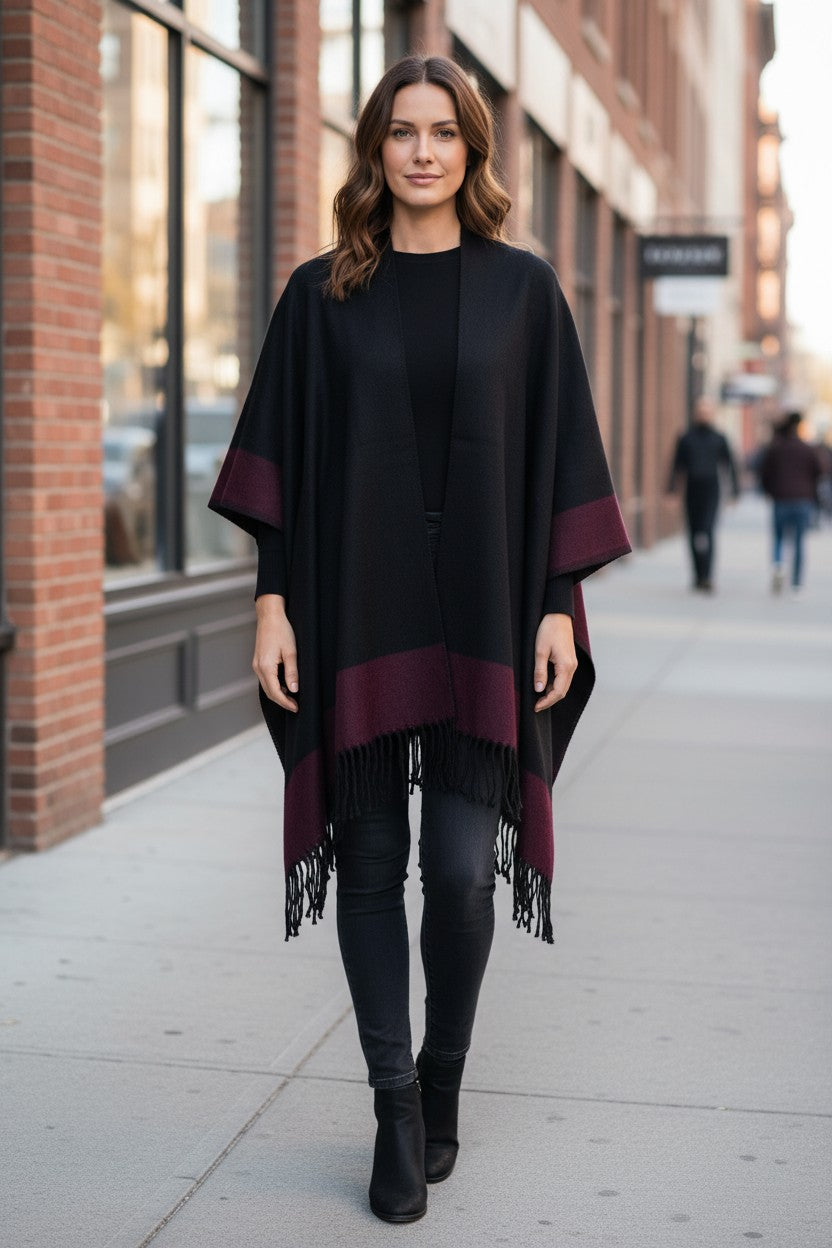 Front view of the reversible black and burgundy wool blend ruana wrap with fringe, styled over an all-black outfit.