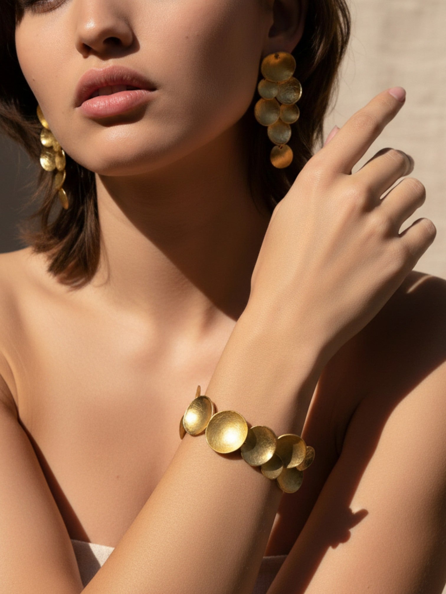 Close-up of gold hammered disc bracelet on wrist, soft sunlight and neutral background