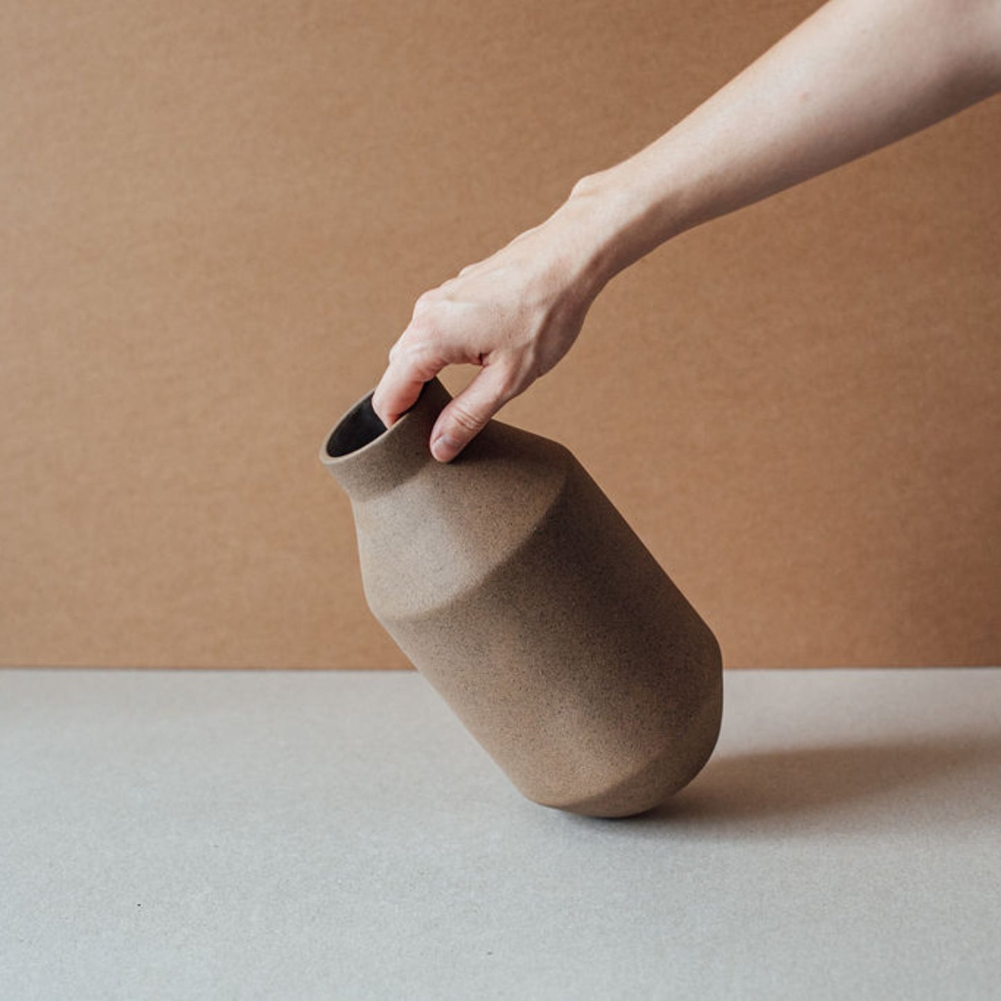 Terracotta chocolate vase tilted in hand showing sculptural geometry and natural clay texture
