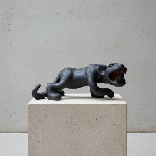 A hand-painted black ceramic reclining Mayan jaguar sculpture displayed on a light stone pedestal against a textured gray wall.
