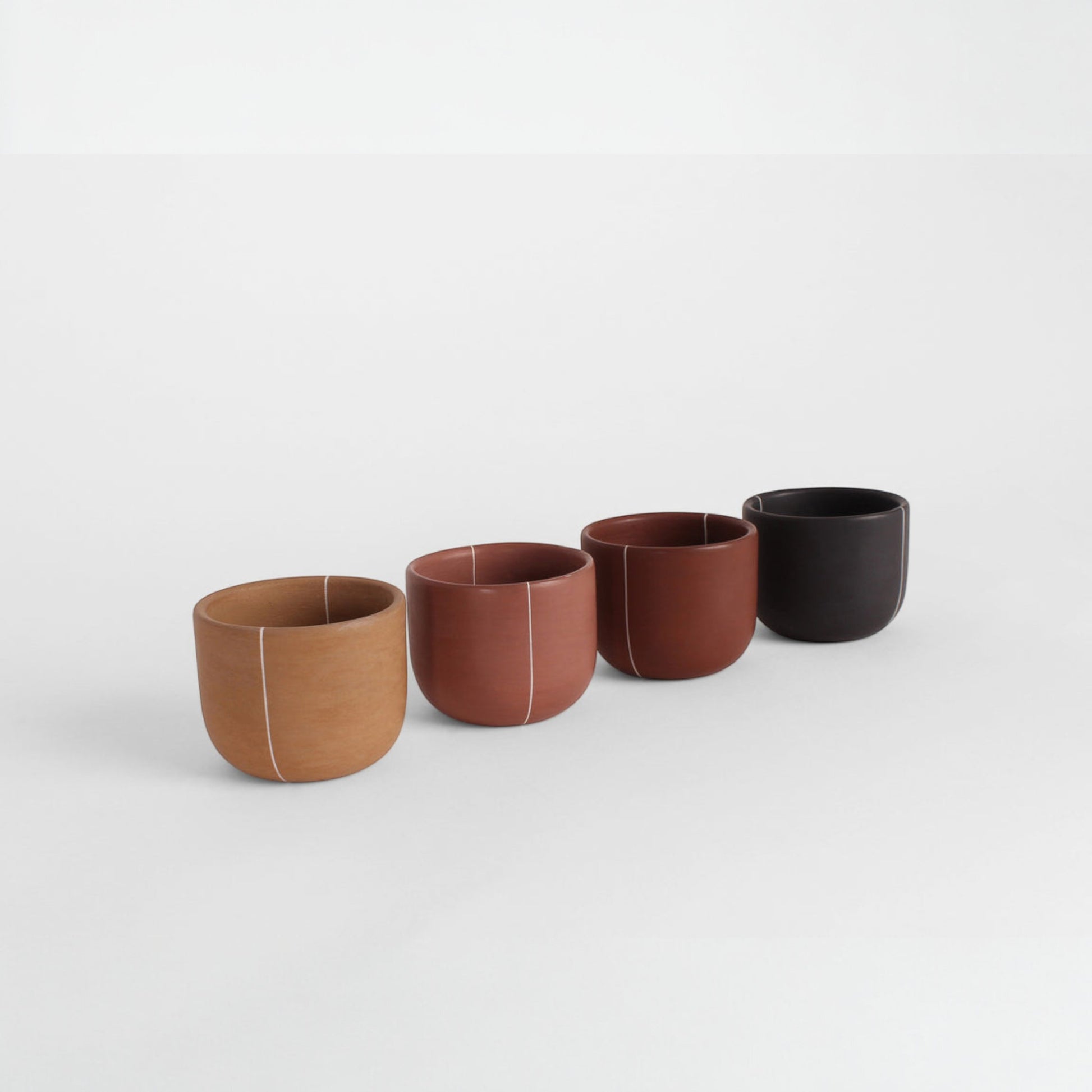 Artisanal burnished clay cups in four colors stacked together on a neutral background