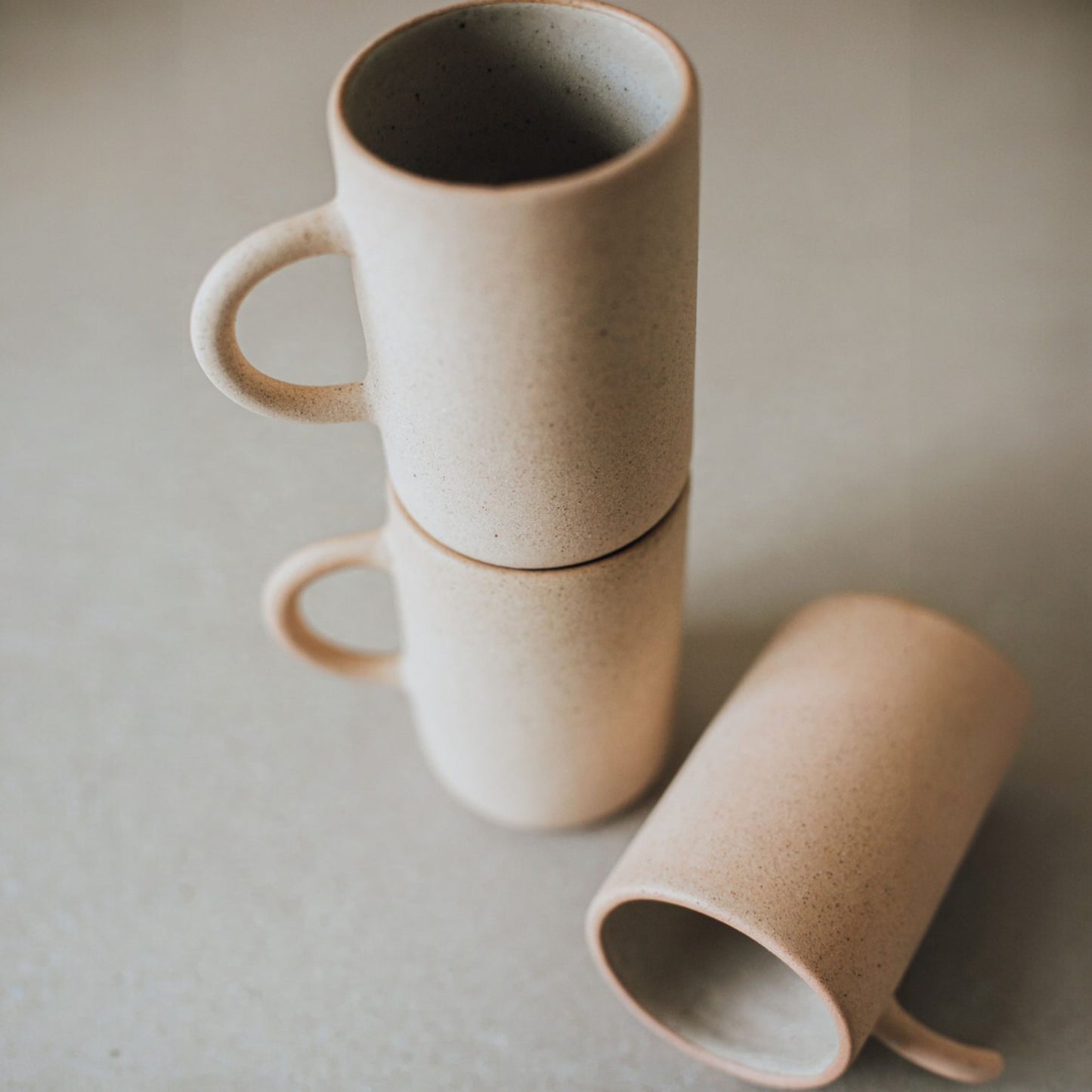 Close-up of three stacked stoneware mugs in beige tones showing texture and organic handcrafted details.