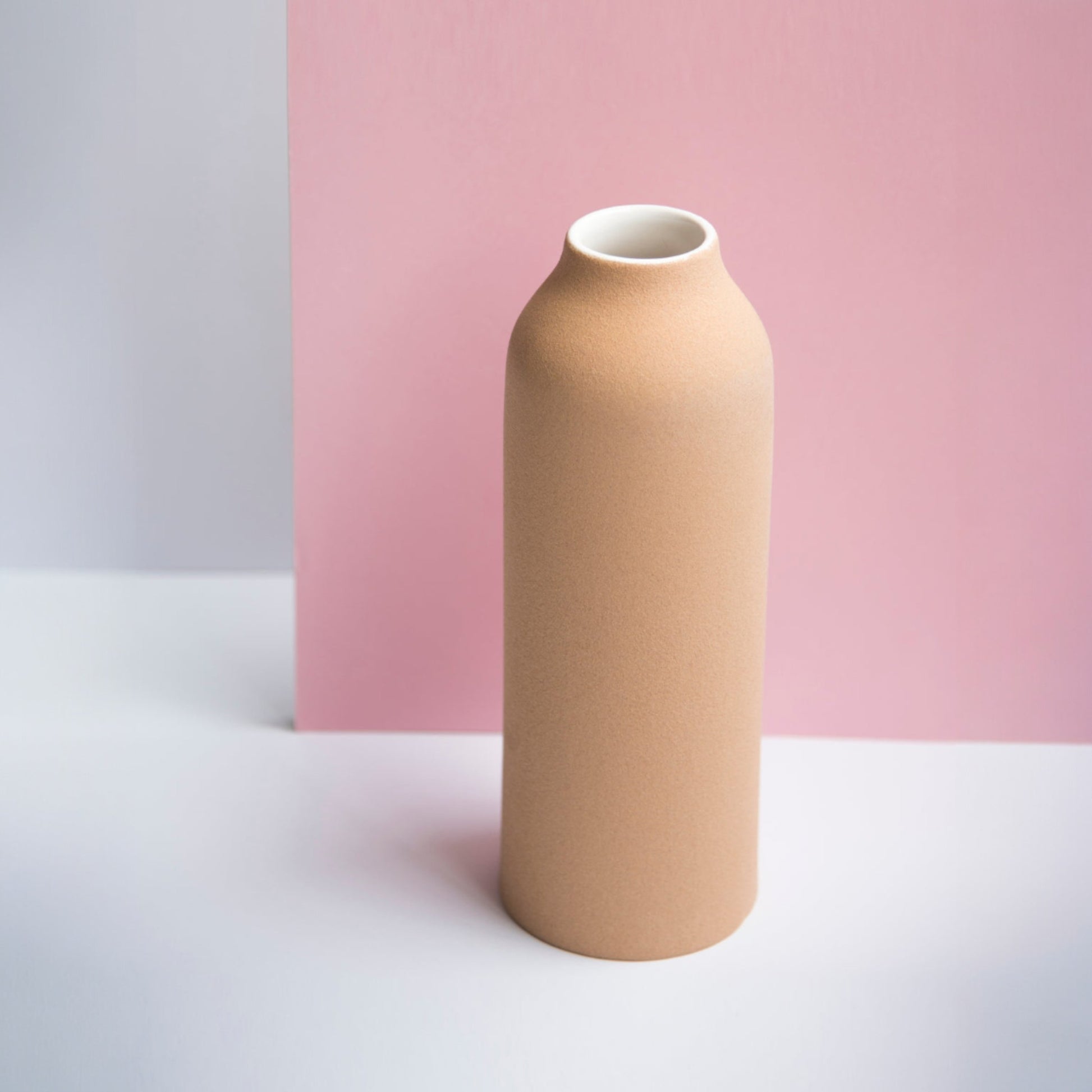 Tall terracotta urn vase with white glaze on a neutral pink background.