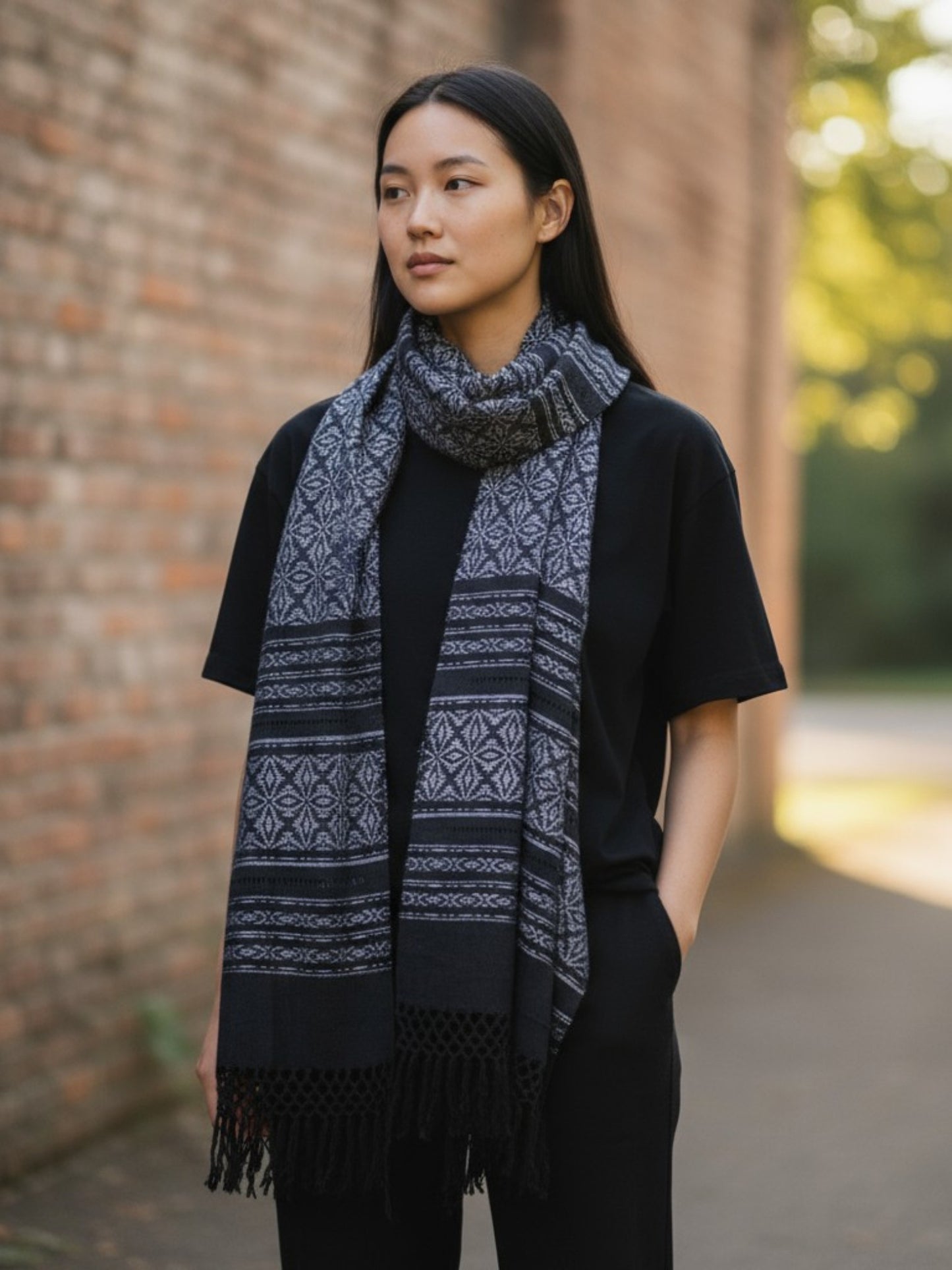 Handwoven charcoal and black cotton rebozo shawl styled as a scarf, featuring traditional Mexican backstrap loom weaving.