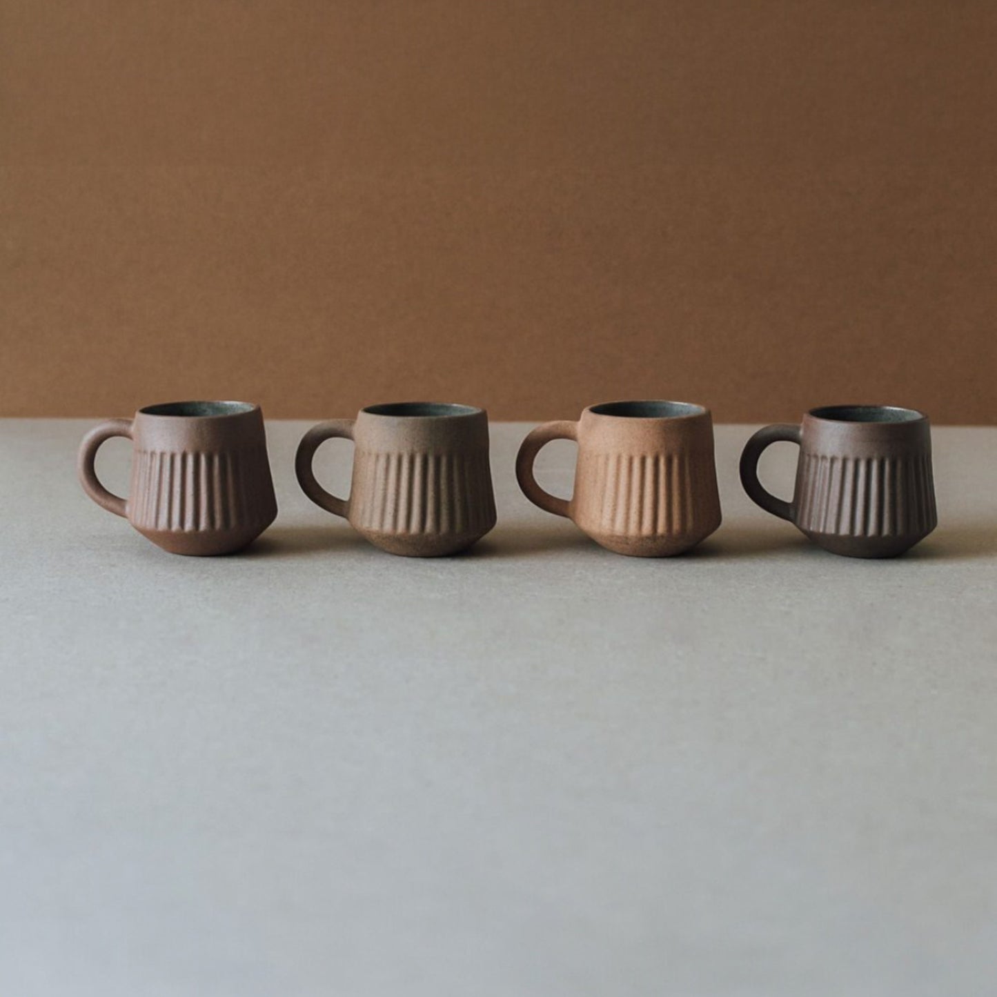 Fluted terracotta mug set arranged in a row, minimalist ceramic coffee cups