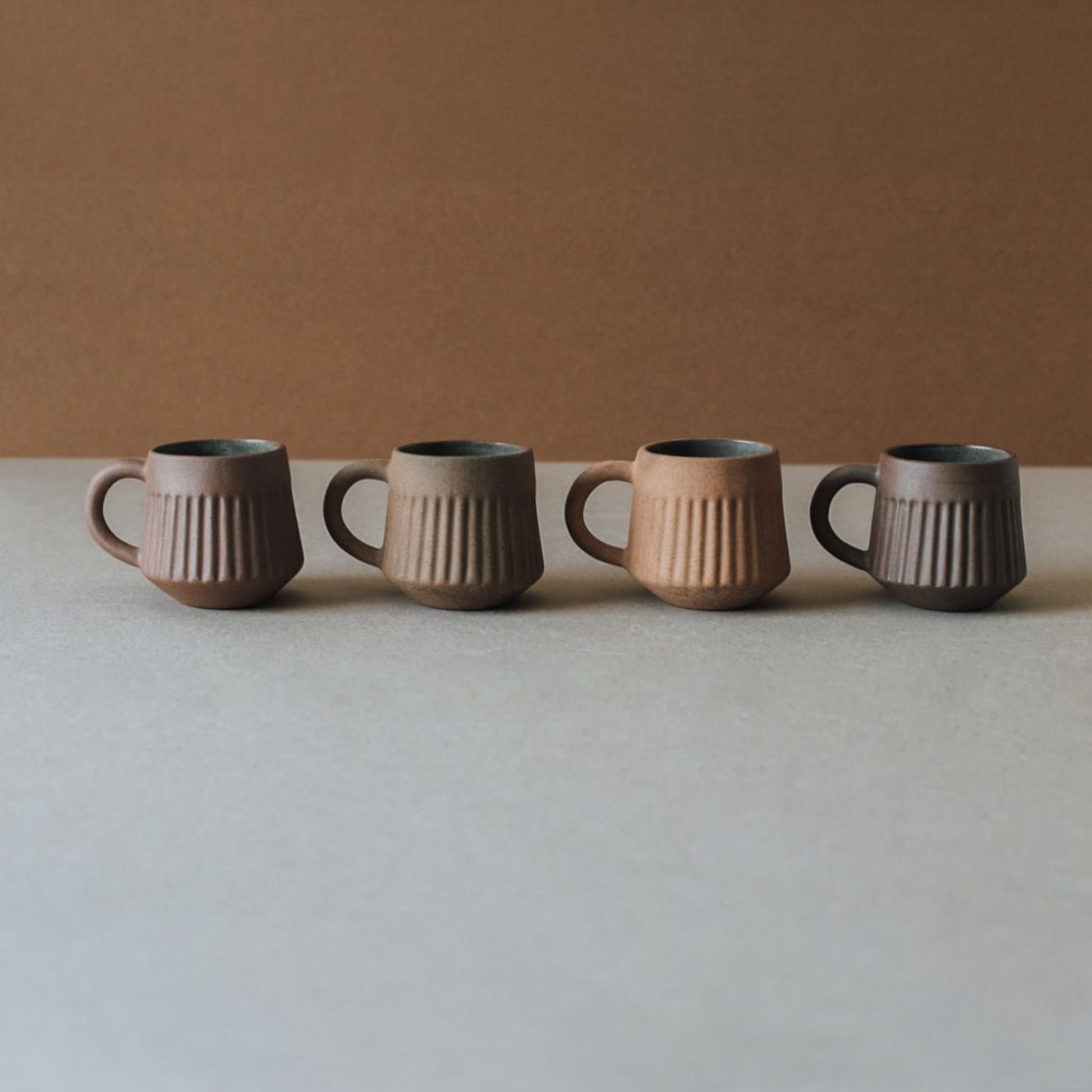 Fluted terracotta mug set arranged in a row, minimalist ceramic coffee cups