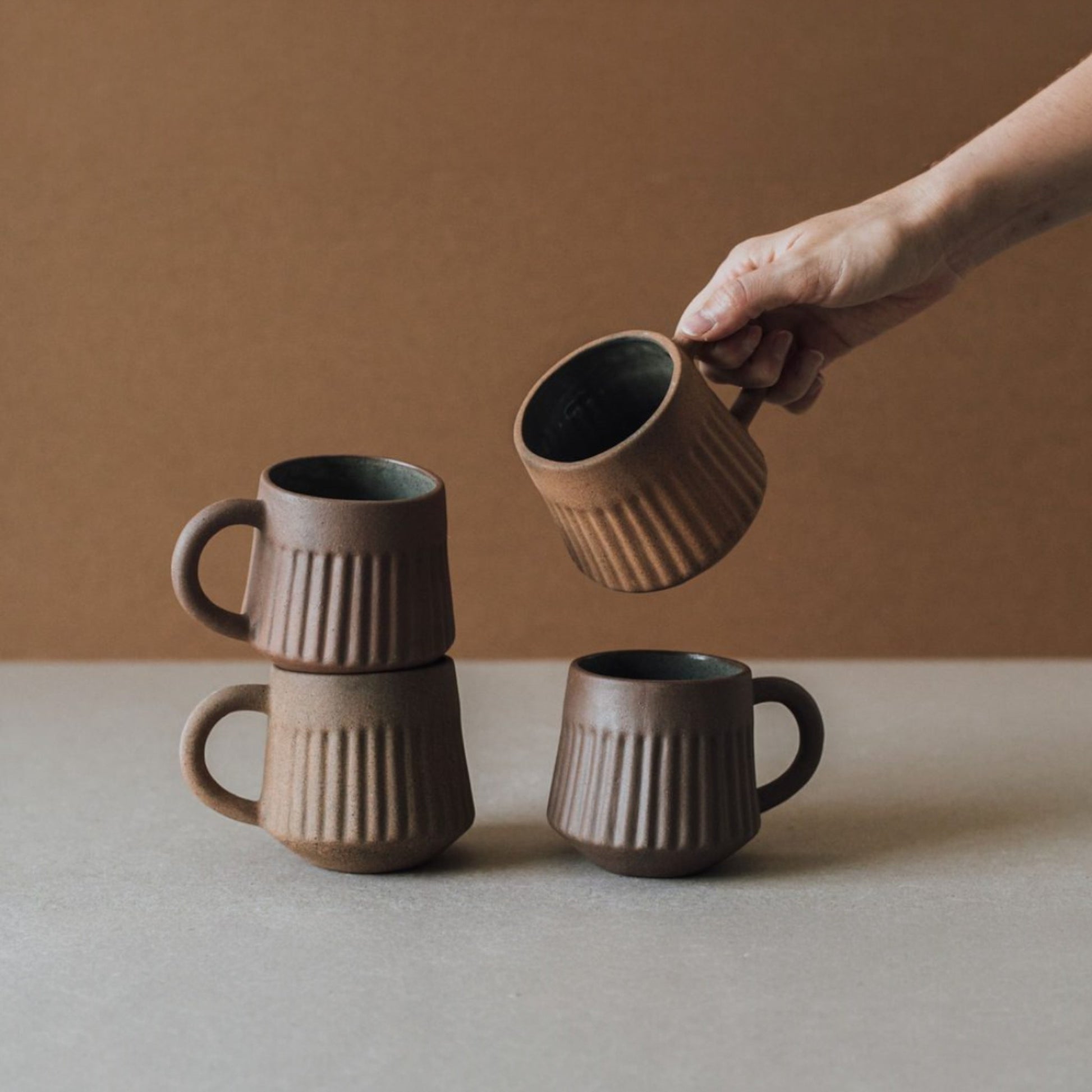 Hand holding fluted terracotta mug with matte ceramic finish