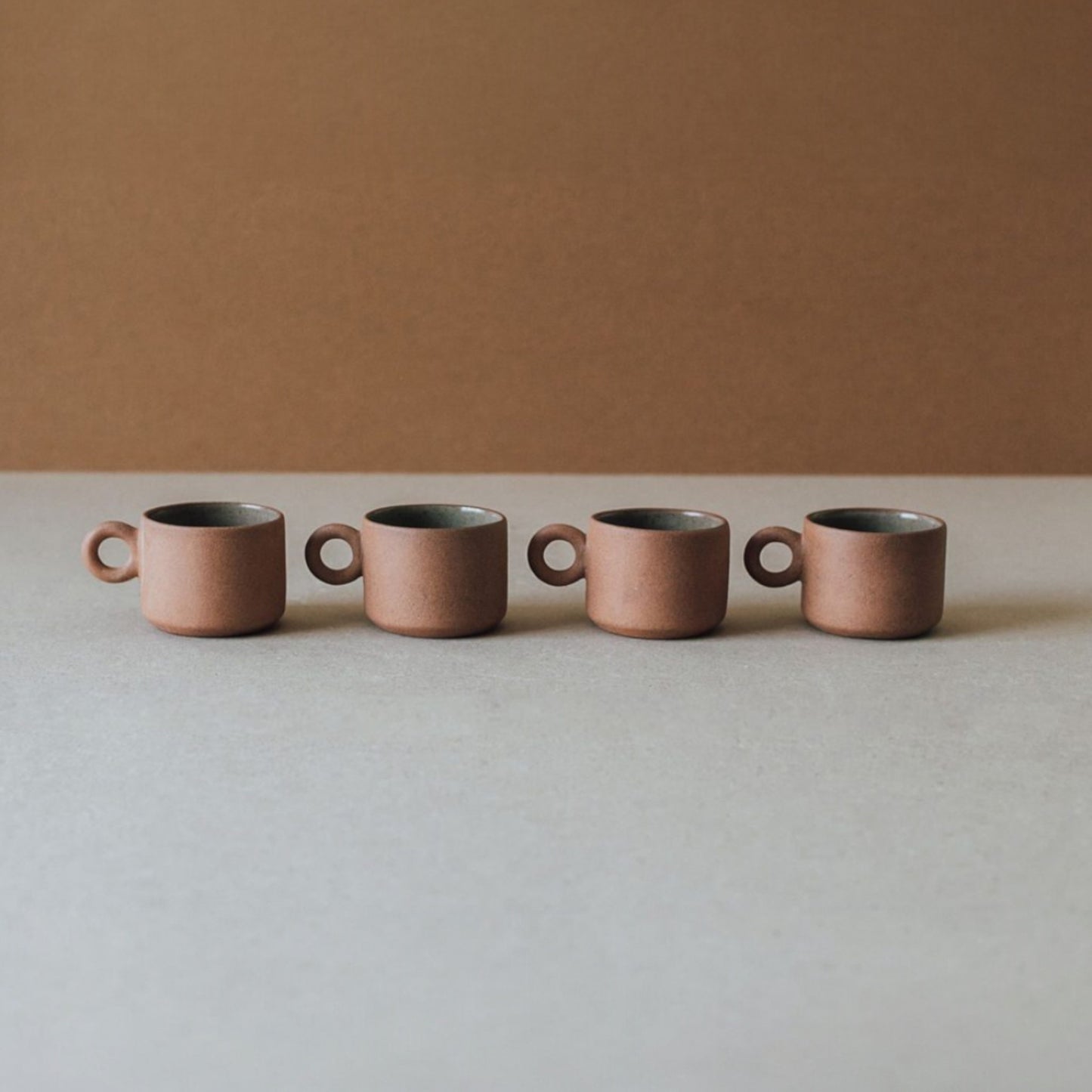Row of small terracotta ceramic cups with ring handles in neutral earthy tones