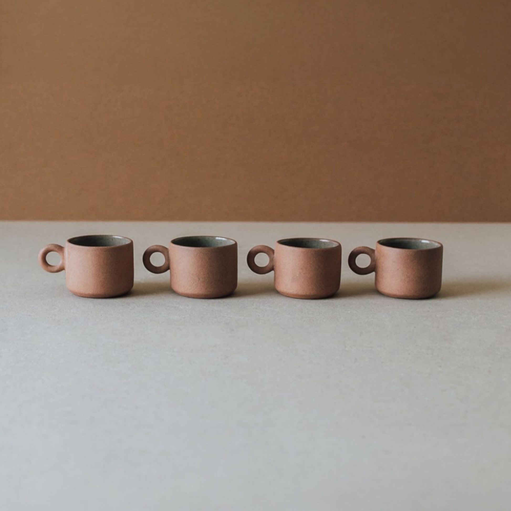 Row of small terracotta ceramic cups with ring handles in neutral earthy tones