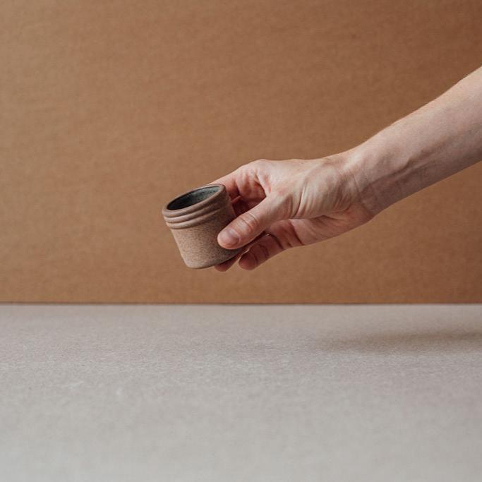 Hand offering a handmade ceramic tequila or mezcal shot glass against a warm-toned background.