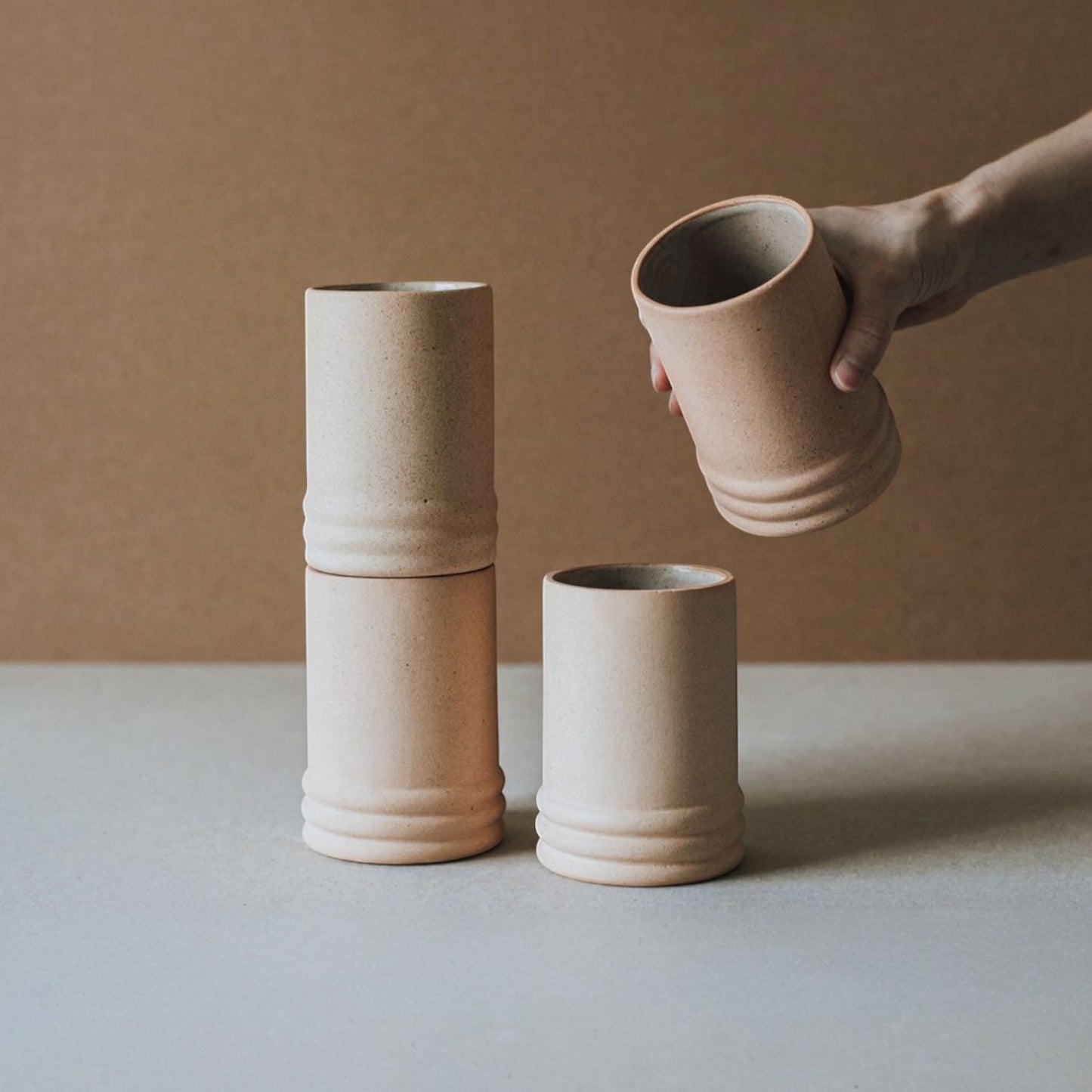 Four beige ceramic cups stacked and arranged on a light surface with a brown background