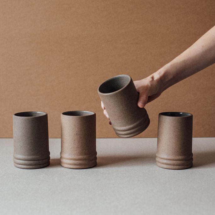 Hand holding a ribbed ceramic cup above three cups on a neutral background
