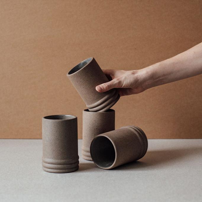 Hand placing a ribbed ceramic cup among four brown ceramic cups on a neutral surface