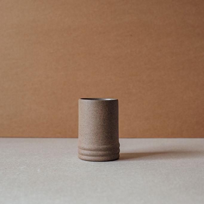Single ribbed ceramic cup on a neutral surface with a brown background