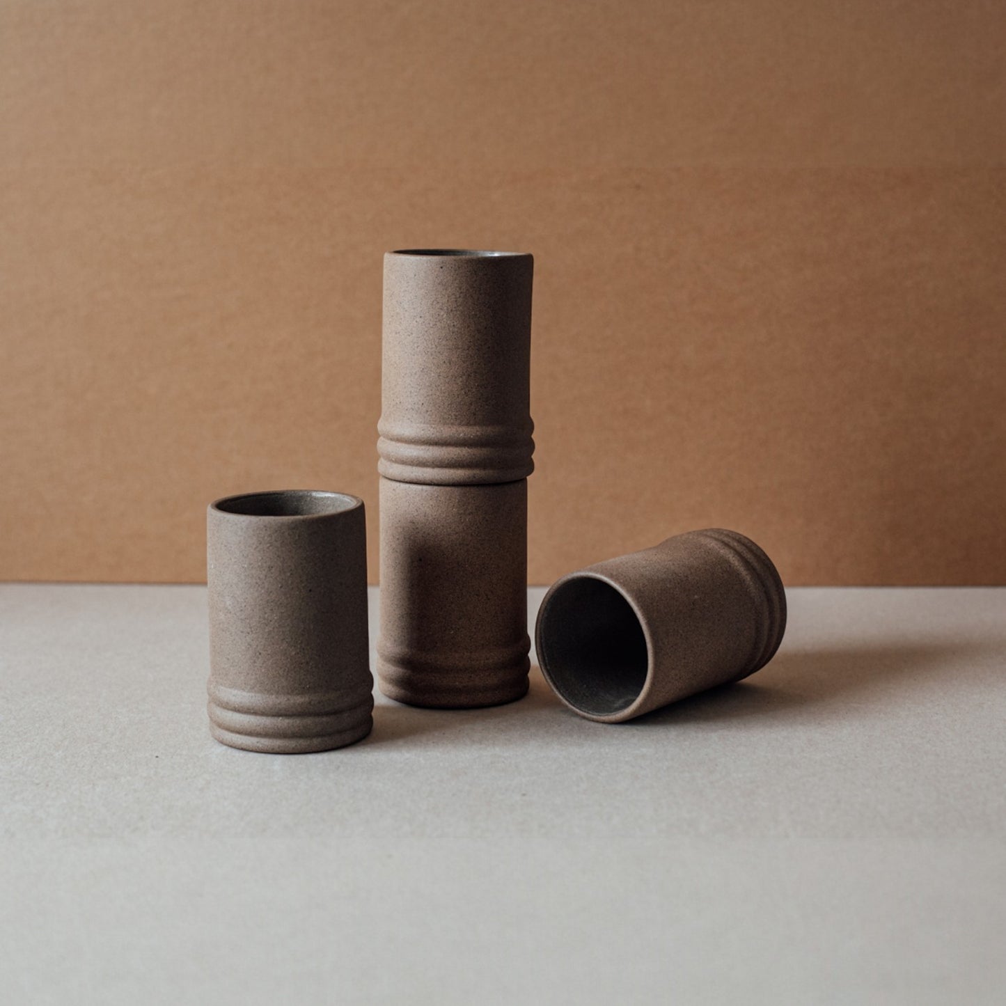 Four brown ceramic cups arranged on a beige surface with a brown background