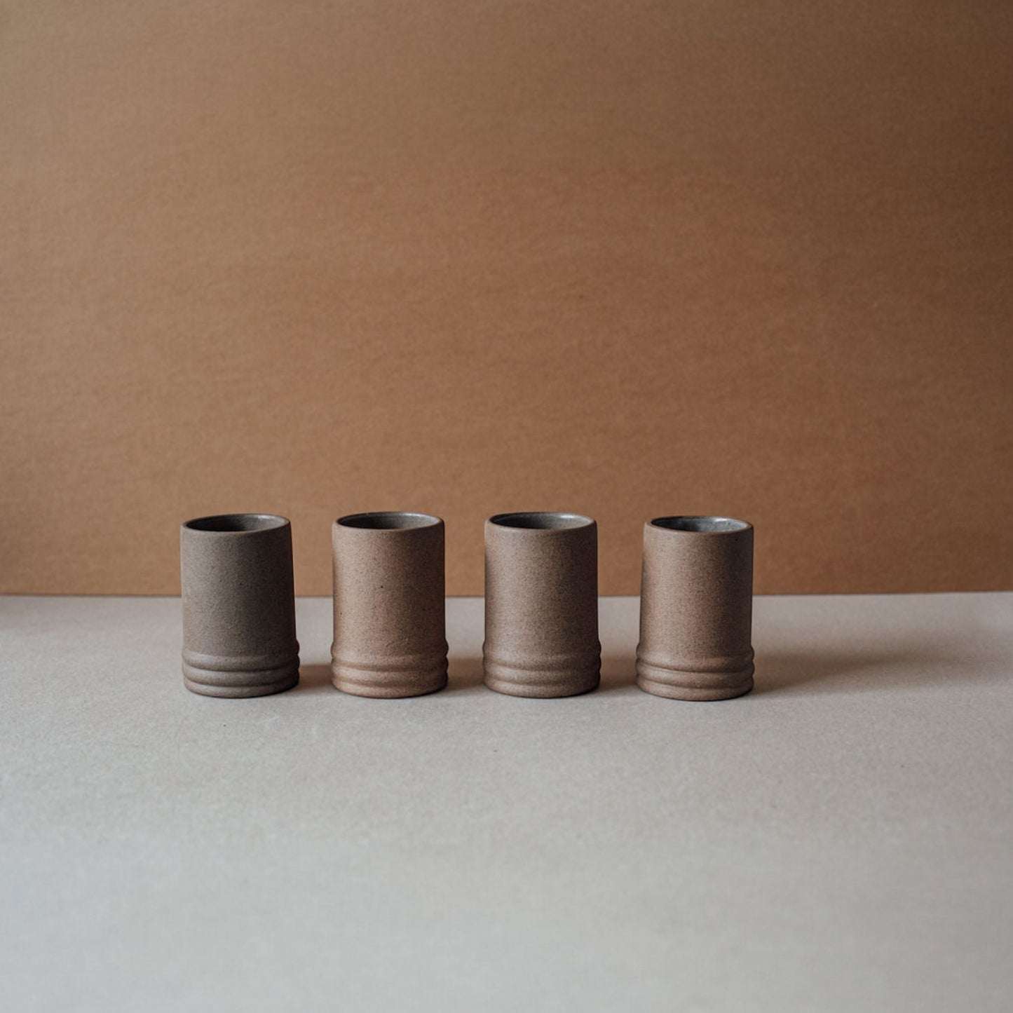 Four ceramic cups in a row on a neutral surface with a brown background