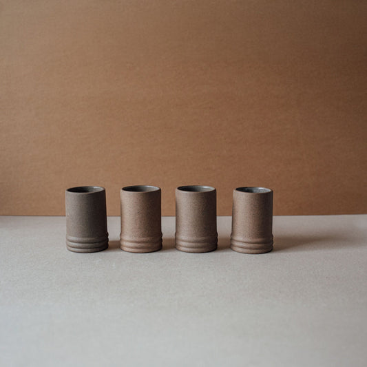 Four ceramic cups in a row on a neutral surface with a brown background
